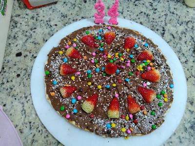 Bolo redondo de chocolate coberto com morangos e confeitos coloridos em um prato branco.