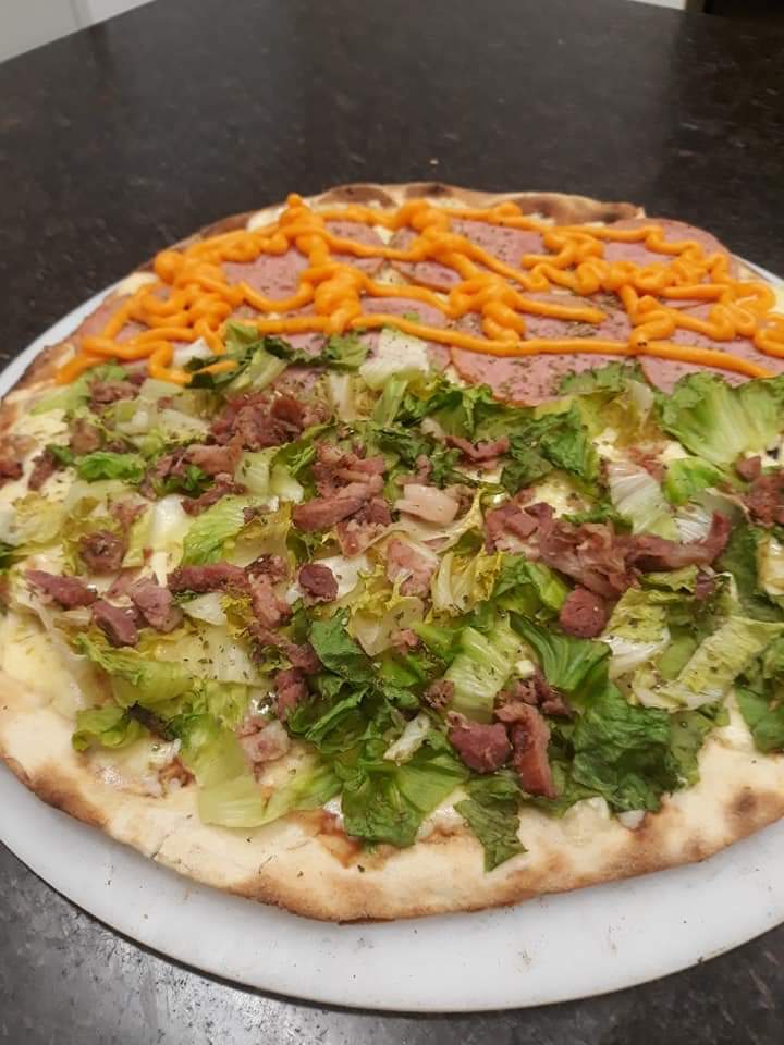 Pizza servida em um prato branco com alface, bacon e molho de laranja por cima.