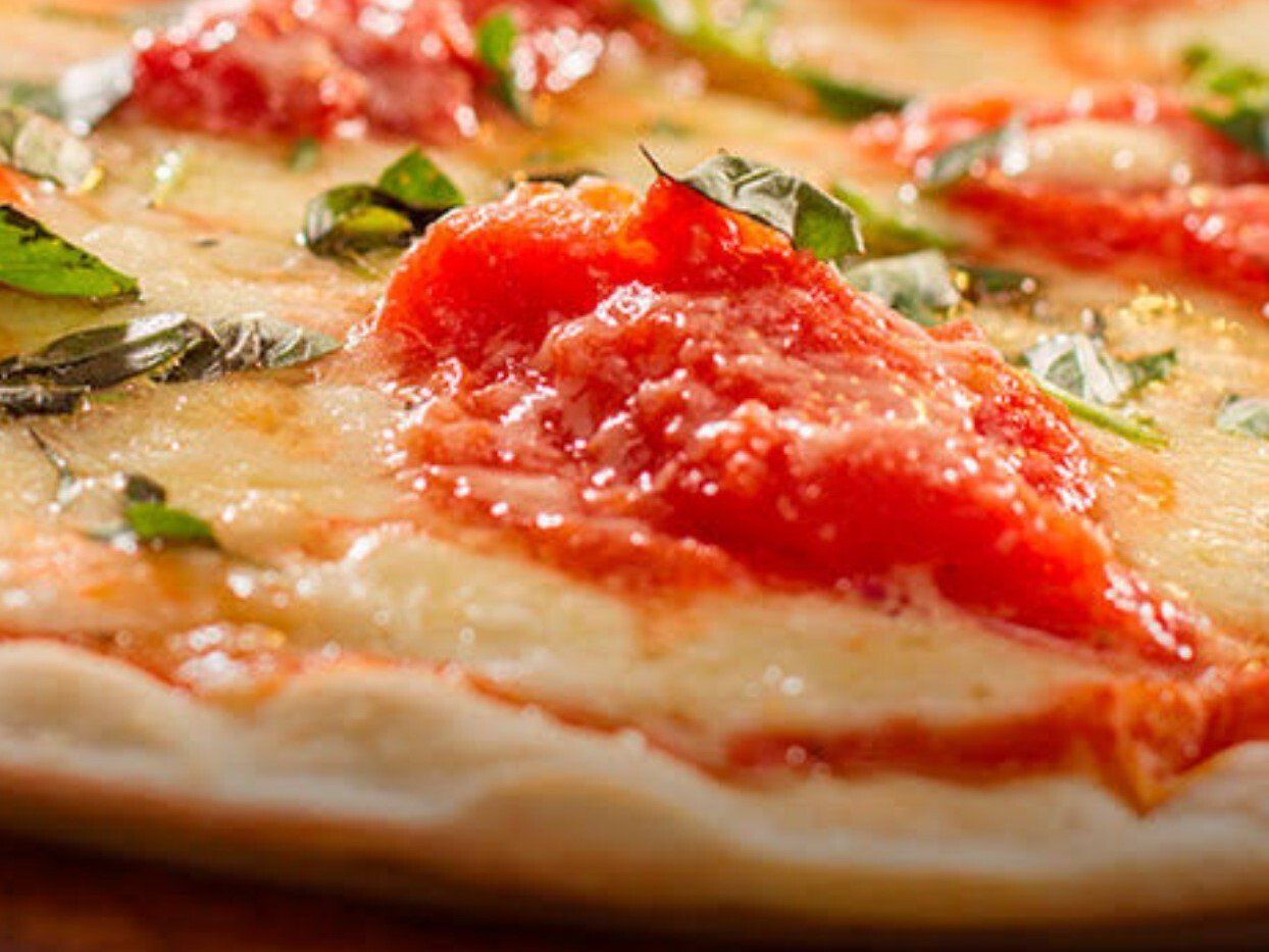Close-up de uma pizza margherita com molho de tomate, queijo derretido e folhas de manjericão sobre uma crosta dourada.