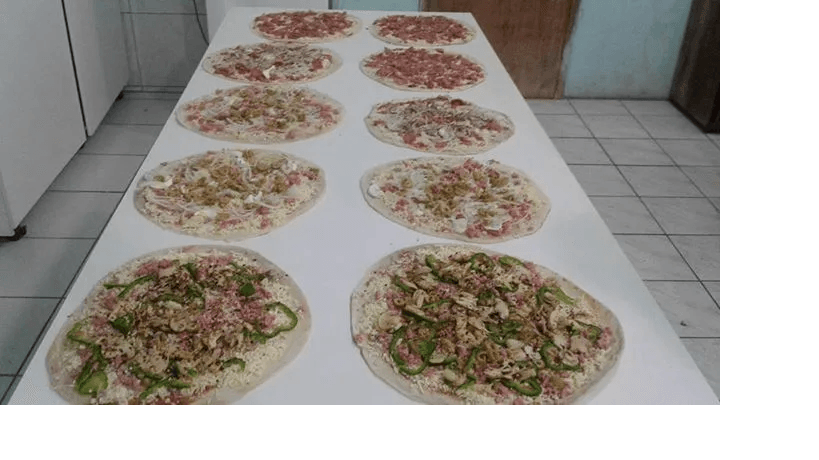 Diversos pratos de salada e outros alimentos dispostos sobre uma longa mesa em uma cozinha revestida de azulejos.