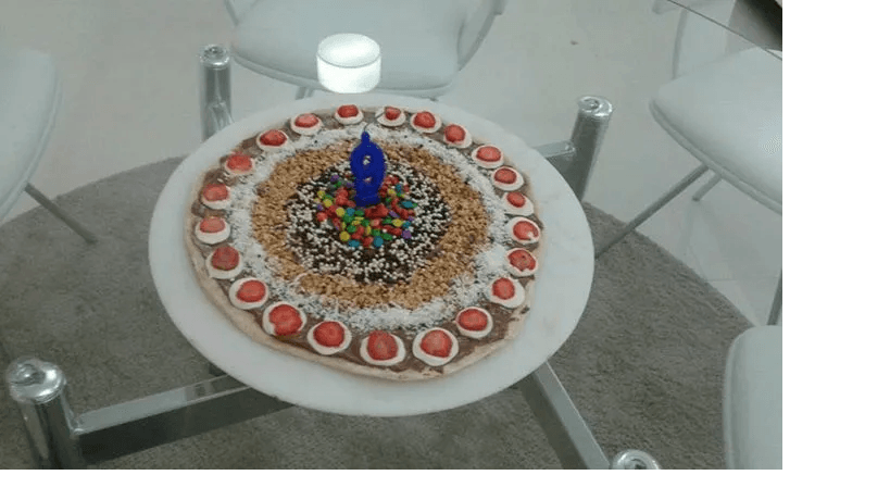 Bolo decorado com morangos e velas sobre uma mesa de vidro em ambiente interno.
