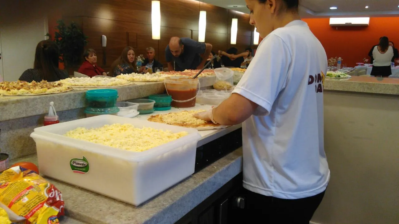 Pessoa servindo comida em um balcão de buffet com bandejas de ingredientes e pratos em uma cafeteria.