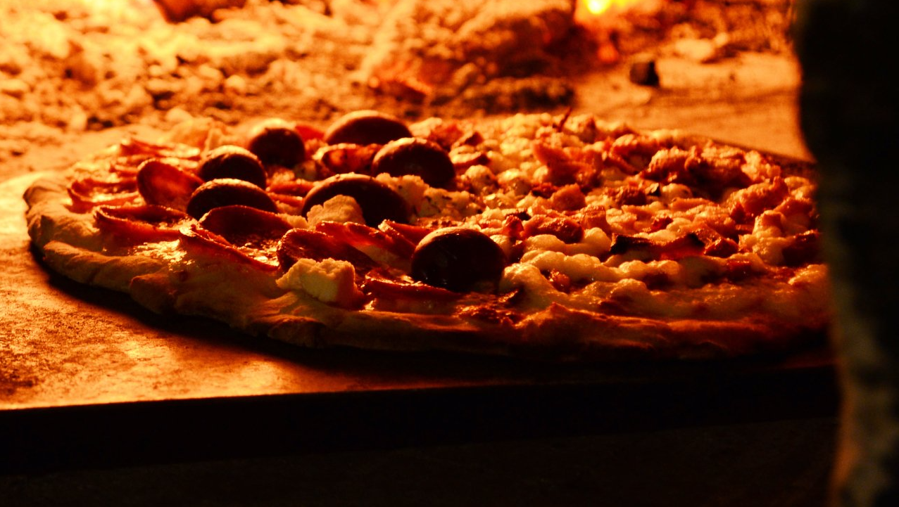 Close-up de uma pizza de pepperoni sobre uma mesa, com iluminação quente e fundo desfocado.