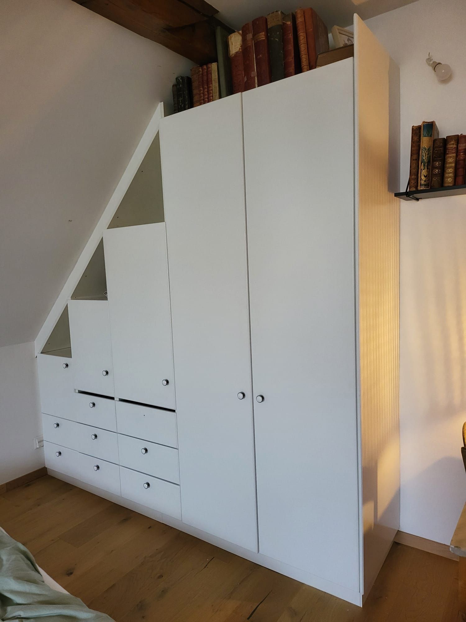 Une armoire blanche avec des escaliers en dessous et des livres sur une étagère.