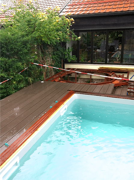 Une piscine avec une terrasse en bois et une maison en arrière-plan