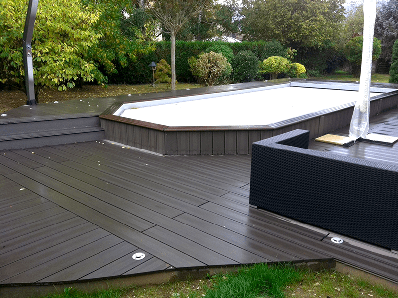 Une terrasse en bois avec une piscine en arrière-plan