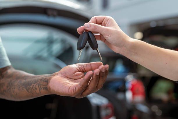 Car keys being handed from one person to another beside a parked car