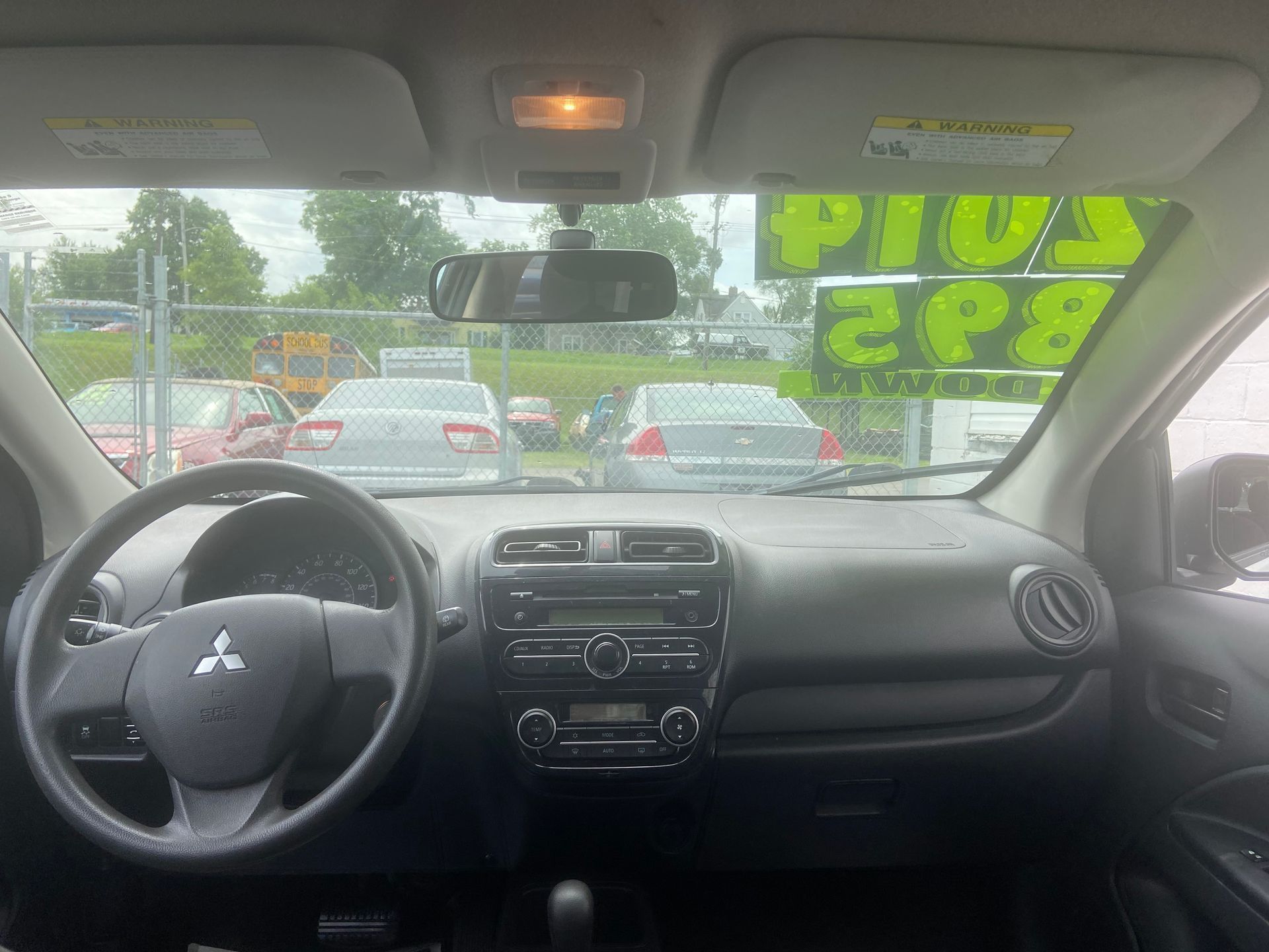 Inside a Mitsubishi car, showing the dashboard and steering wheel, with traffic visible through the windshield.