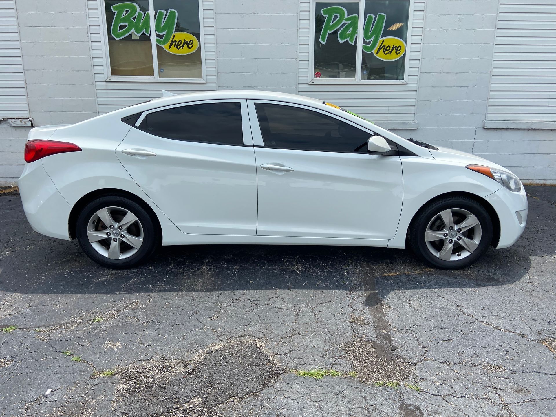 White sedan parked outside a building with Buy Here signs in the windows.