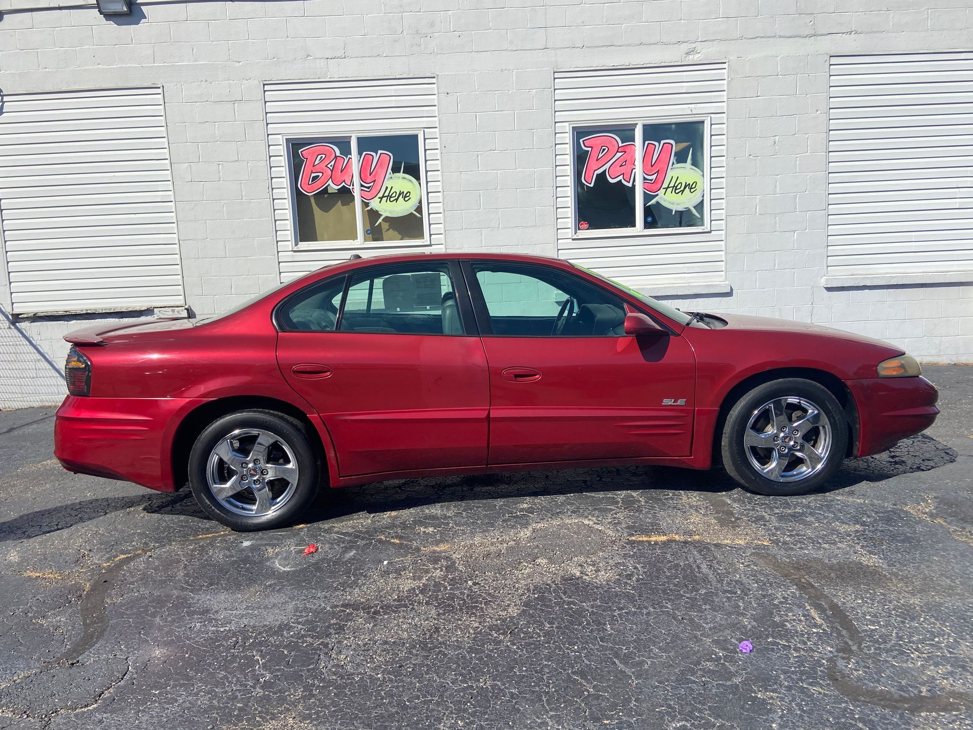 Red sports coupe parked beside a white building with windows and a textured facade.