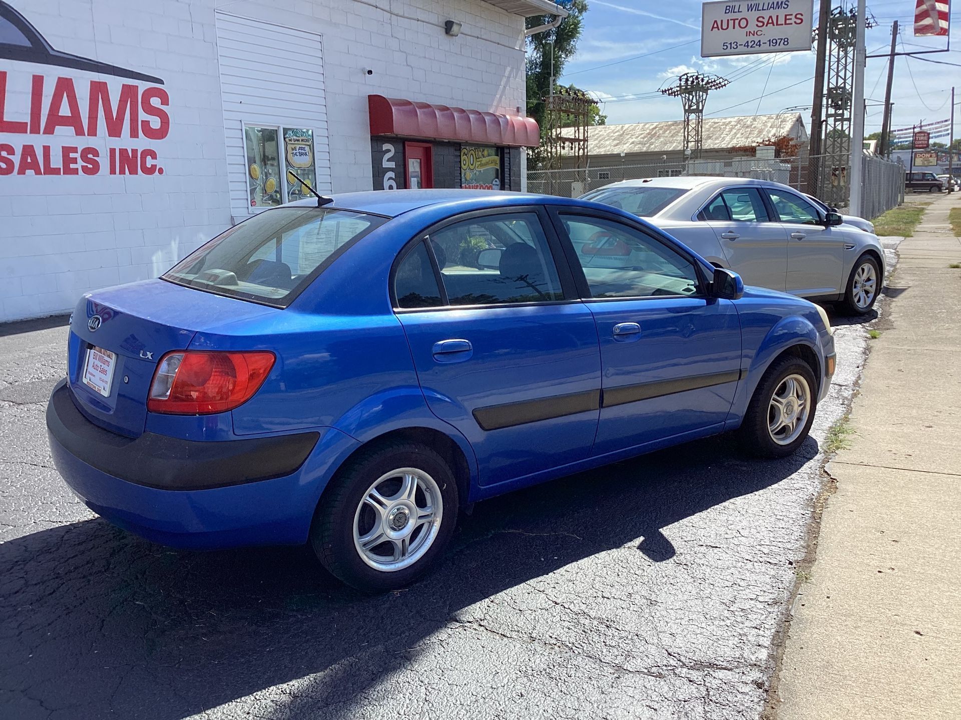 Blue sedan parked outside a car sales lot beside a silver car on a sunny day