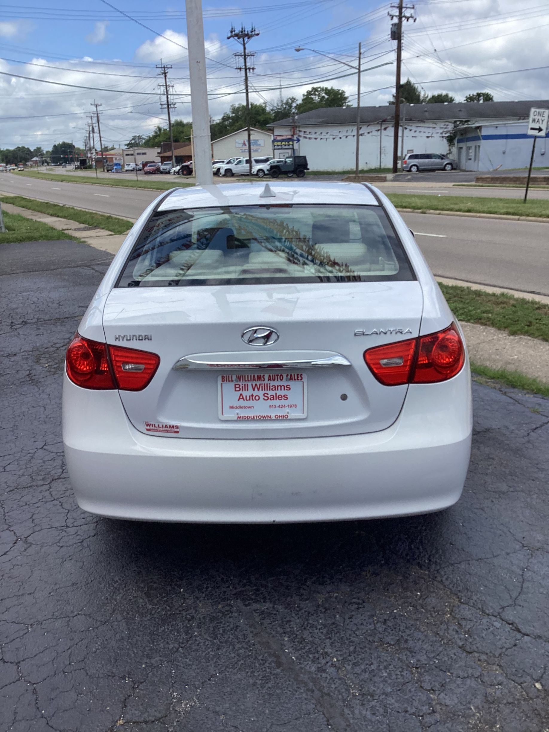 Silver sedan parked on a wet lot, with bright yellow price and model-year stickers on the windshield.