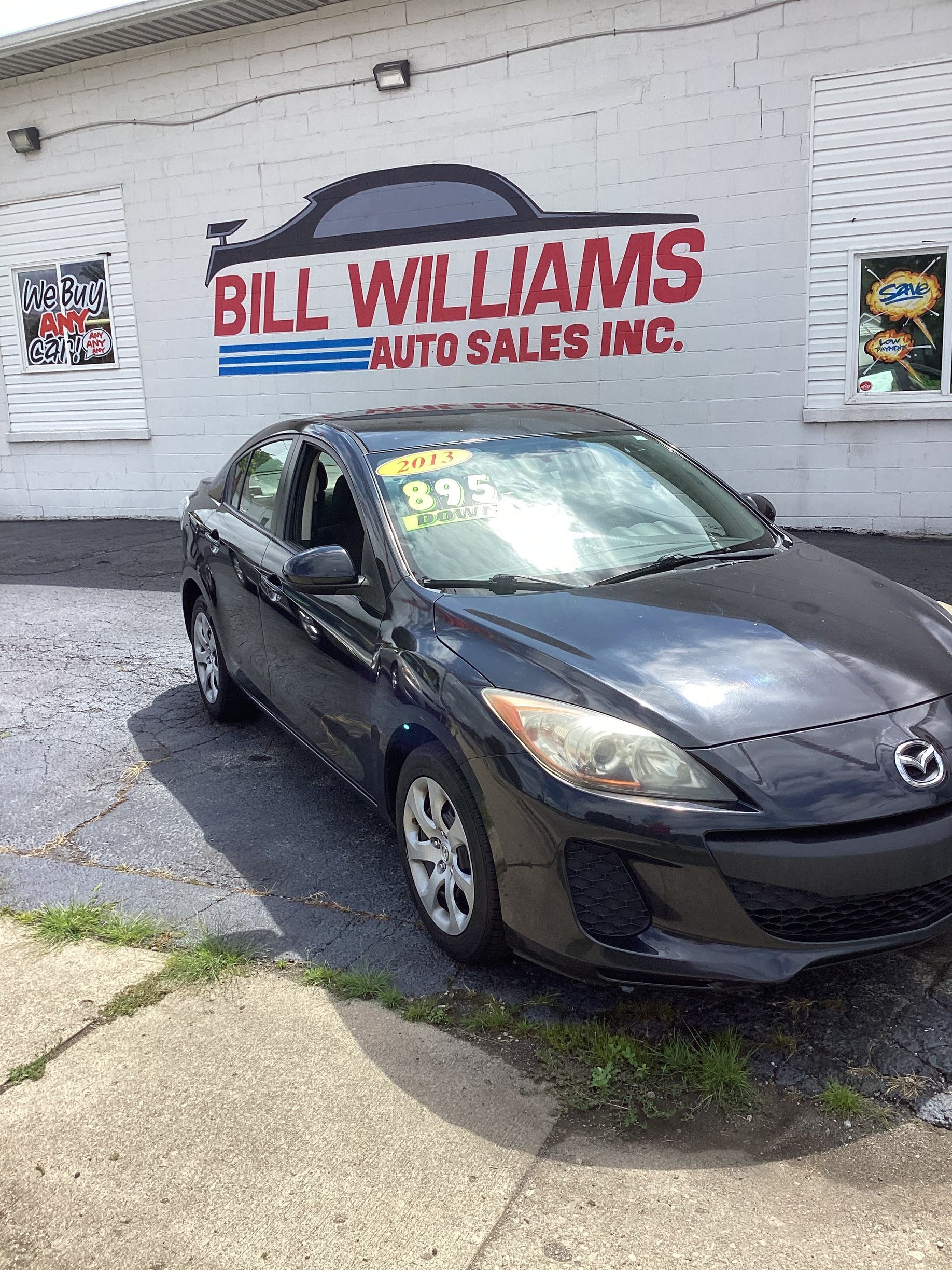 Black sedan parked by Bill Williams Auto Sales with price written on the windshield.