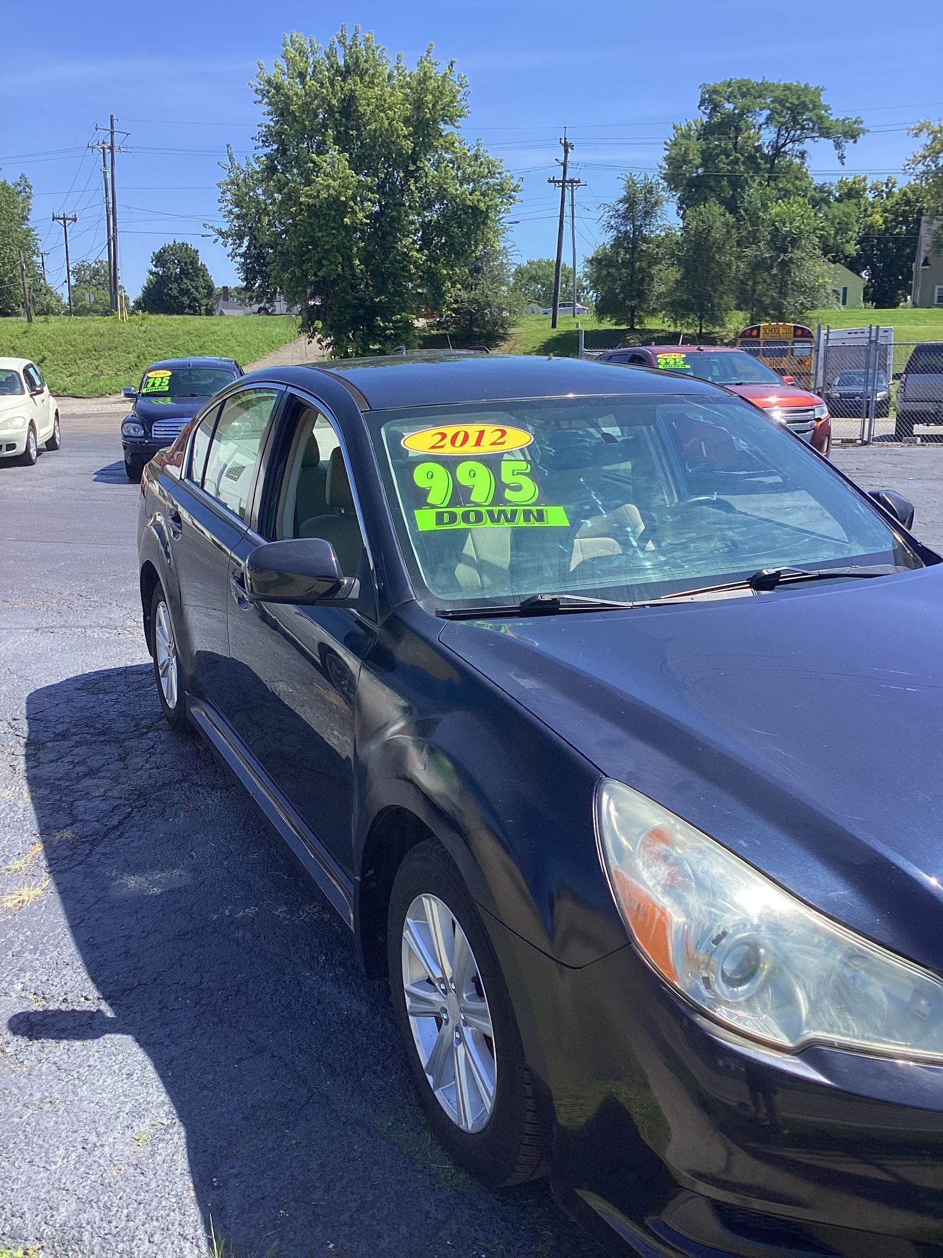 Silver sedan parked on a wet lot, with bright yellow price and model-year stickers on the windshield.