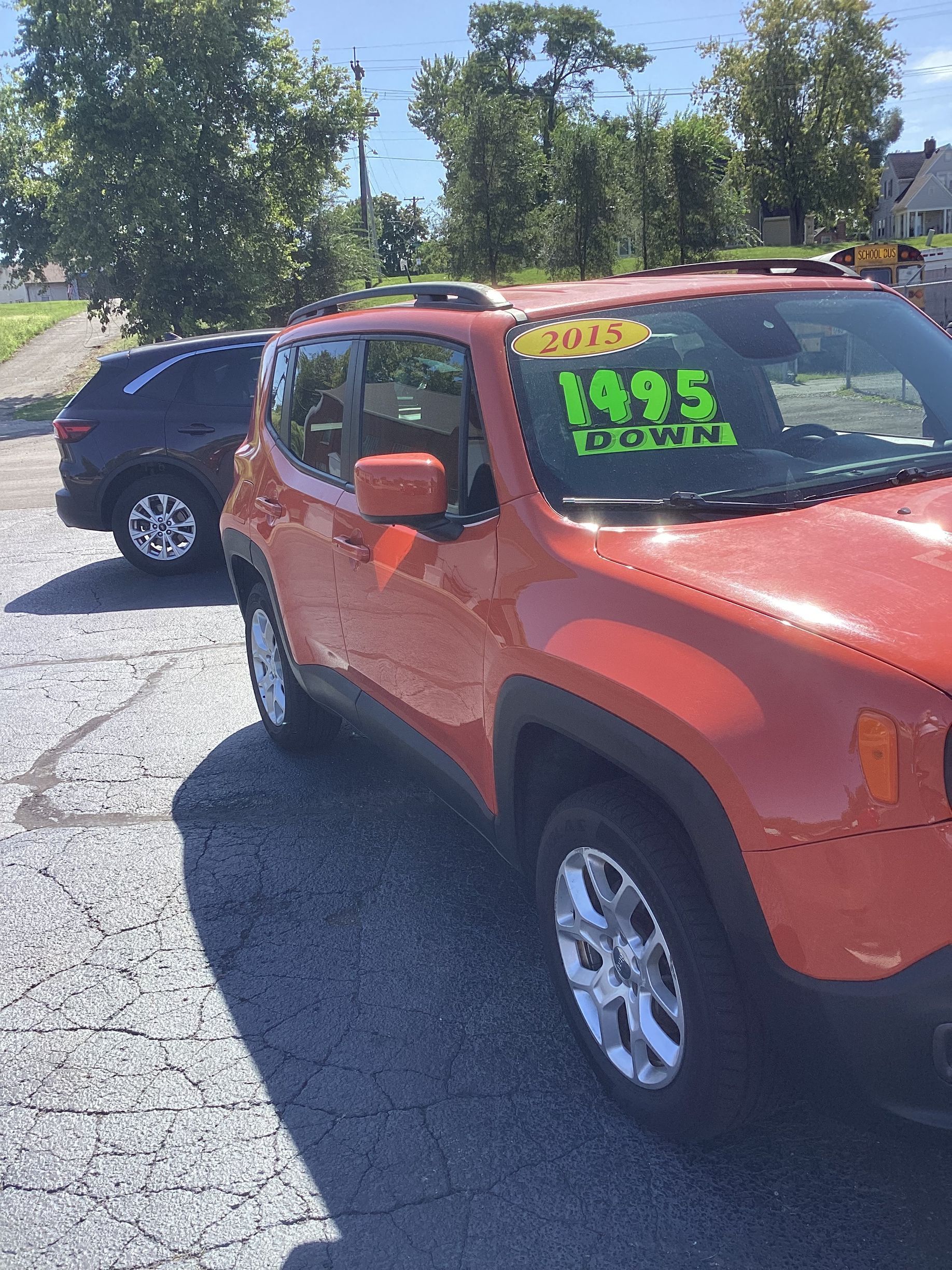 Red SUV with neon green price signs parked on a wet lot near a brick building