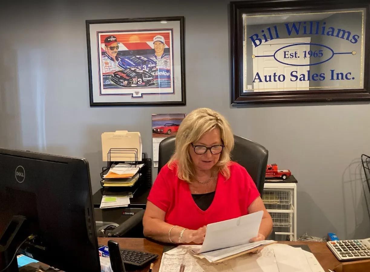 Woman in red shirt reviewing papers at a desk in an auto sales office Woman in red shirt reviewing papers at a desk in an auto sales office