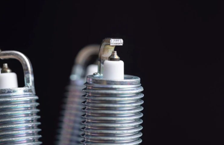Close-up of two spark plugs against a dark background, with one in sharp focus.