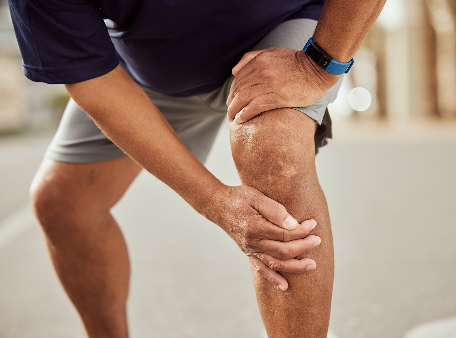 Person holding a sore knee while standing in athletic shorts, suggesting knee pain or injury