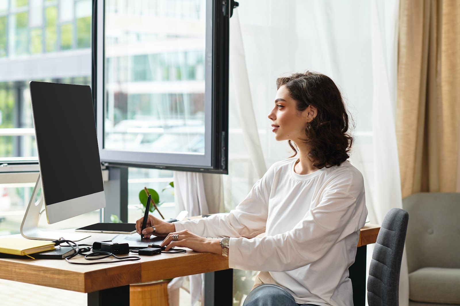 Person working at a desk by a large window, using a desktop computer in a bright office