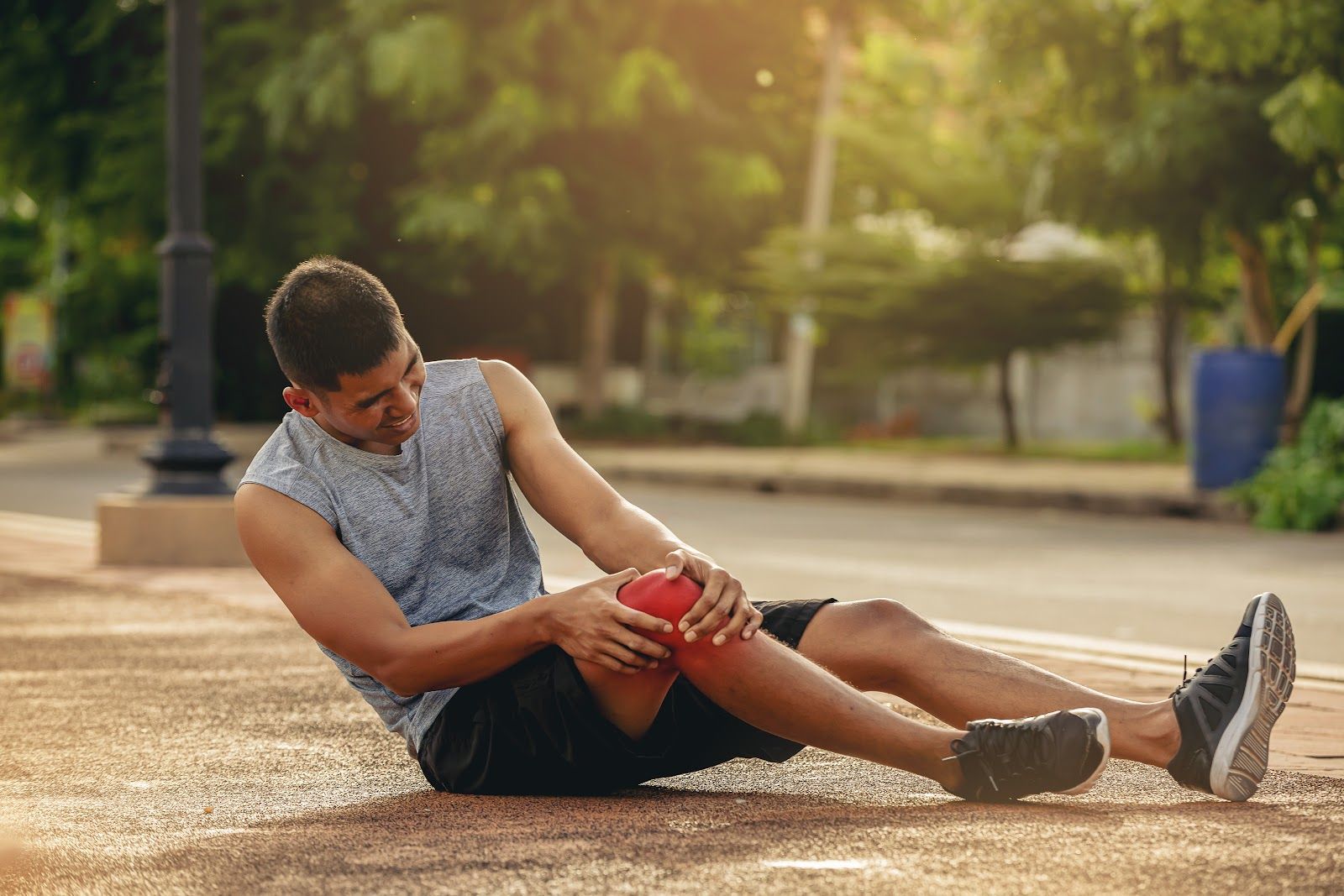 Man sitting on a track, holding his knee in pain while resting outdoors at sunset