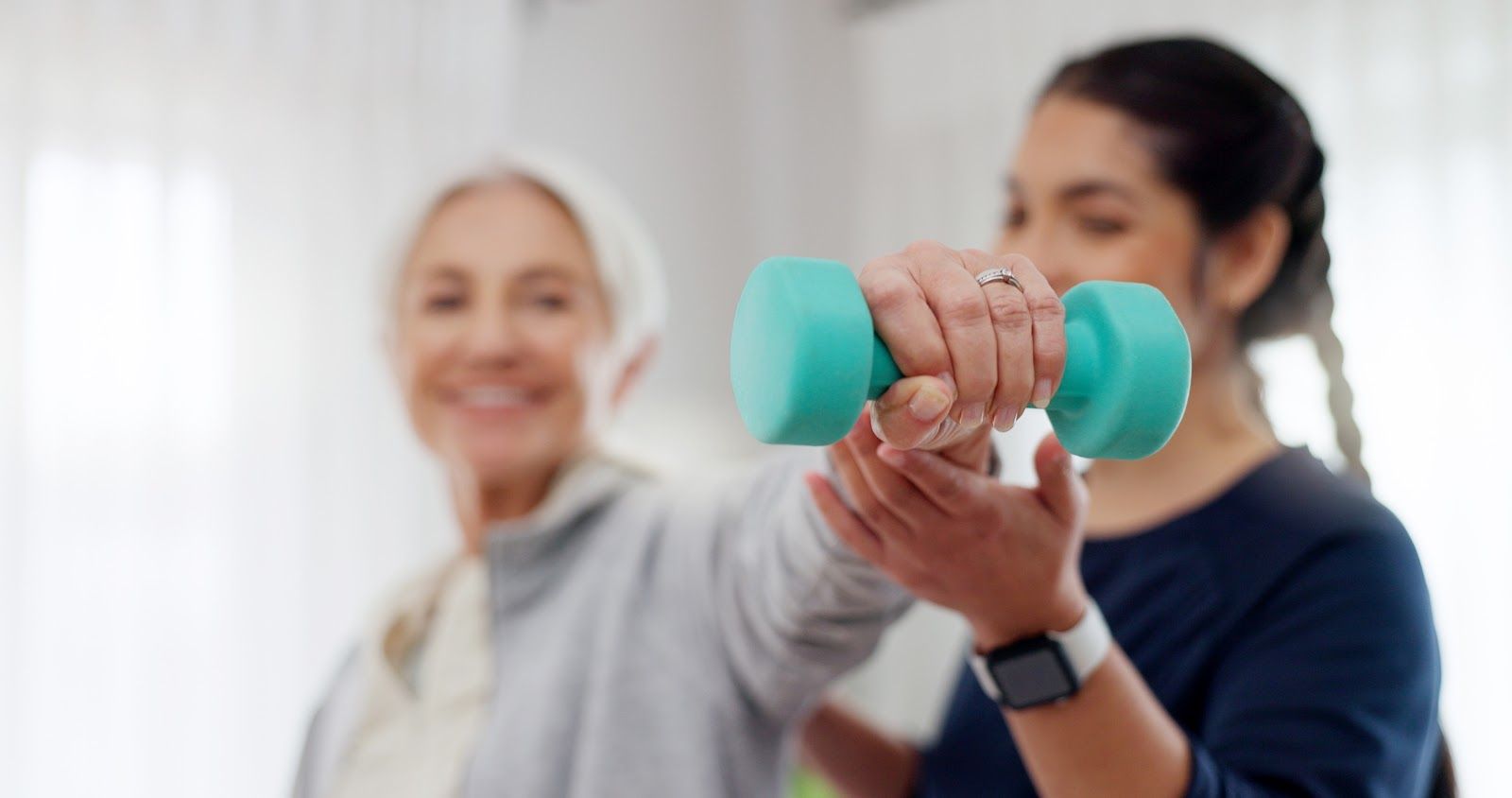 Two people exercise with a turquoise dumbbell, one guiding the other in a bright indoor setting