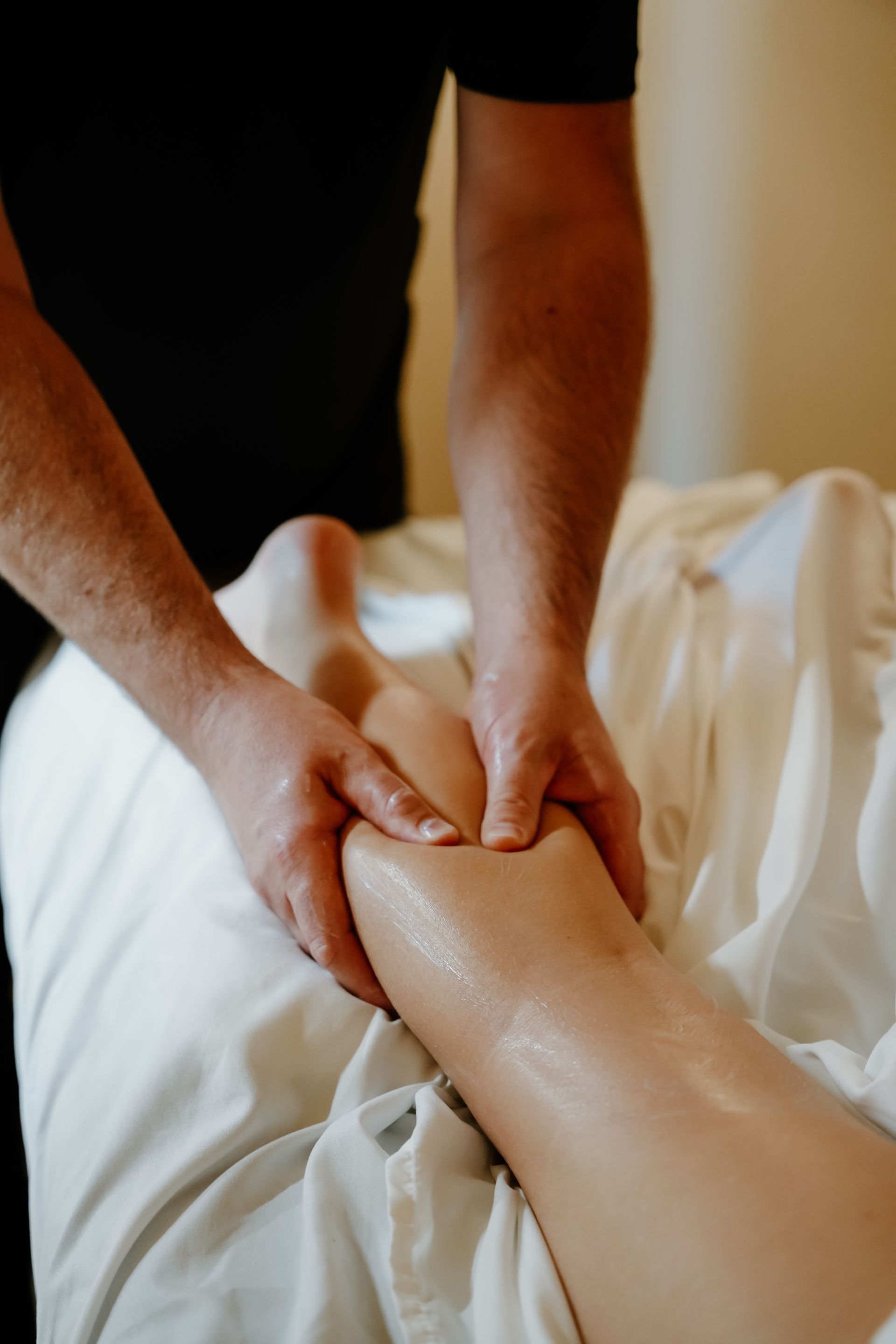 Hands massaging a person’s calf and foot on a white towel, spa setting