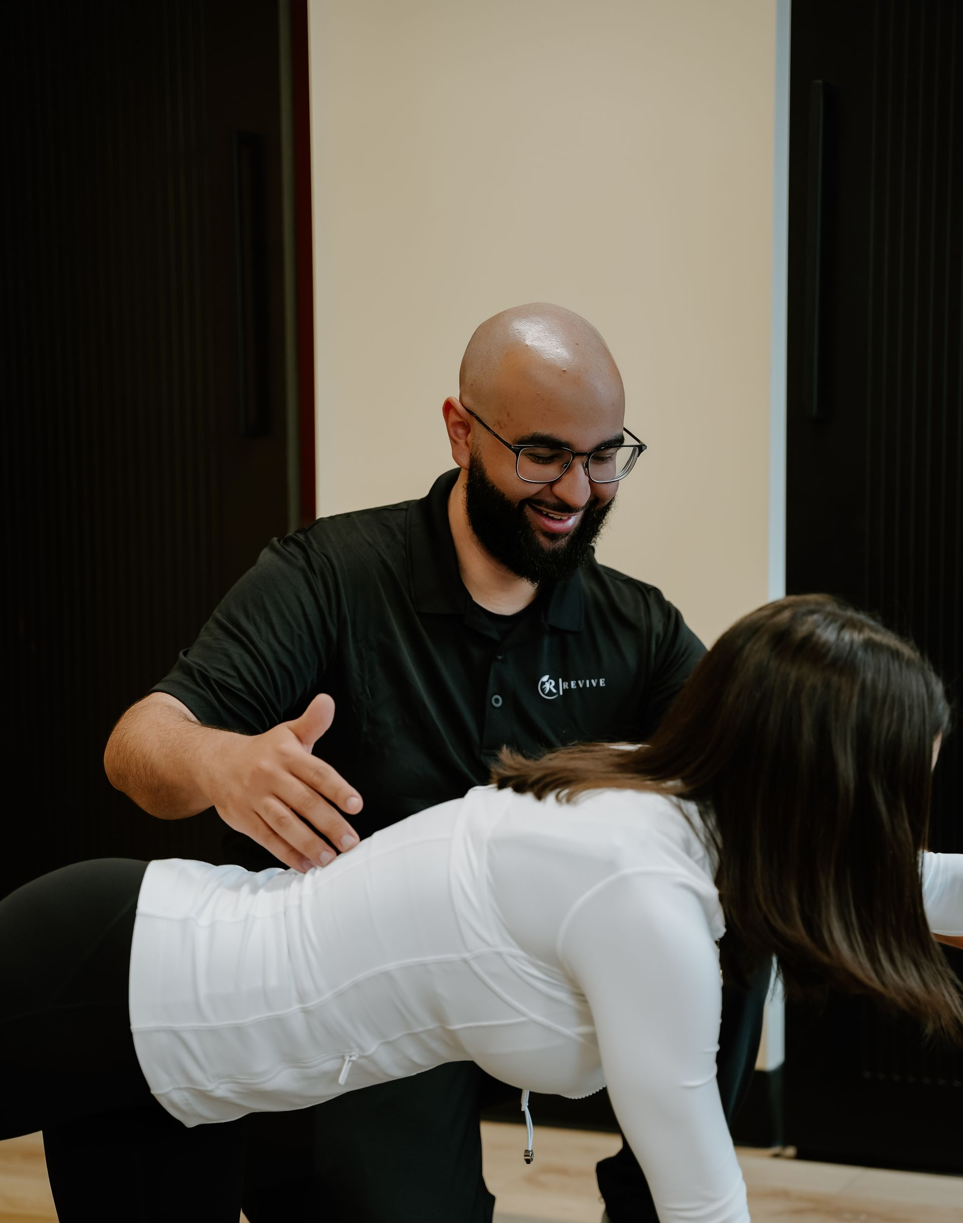 Trainer assisting a person in white shirt doing a floor exercise indoors