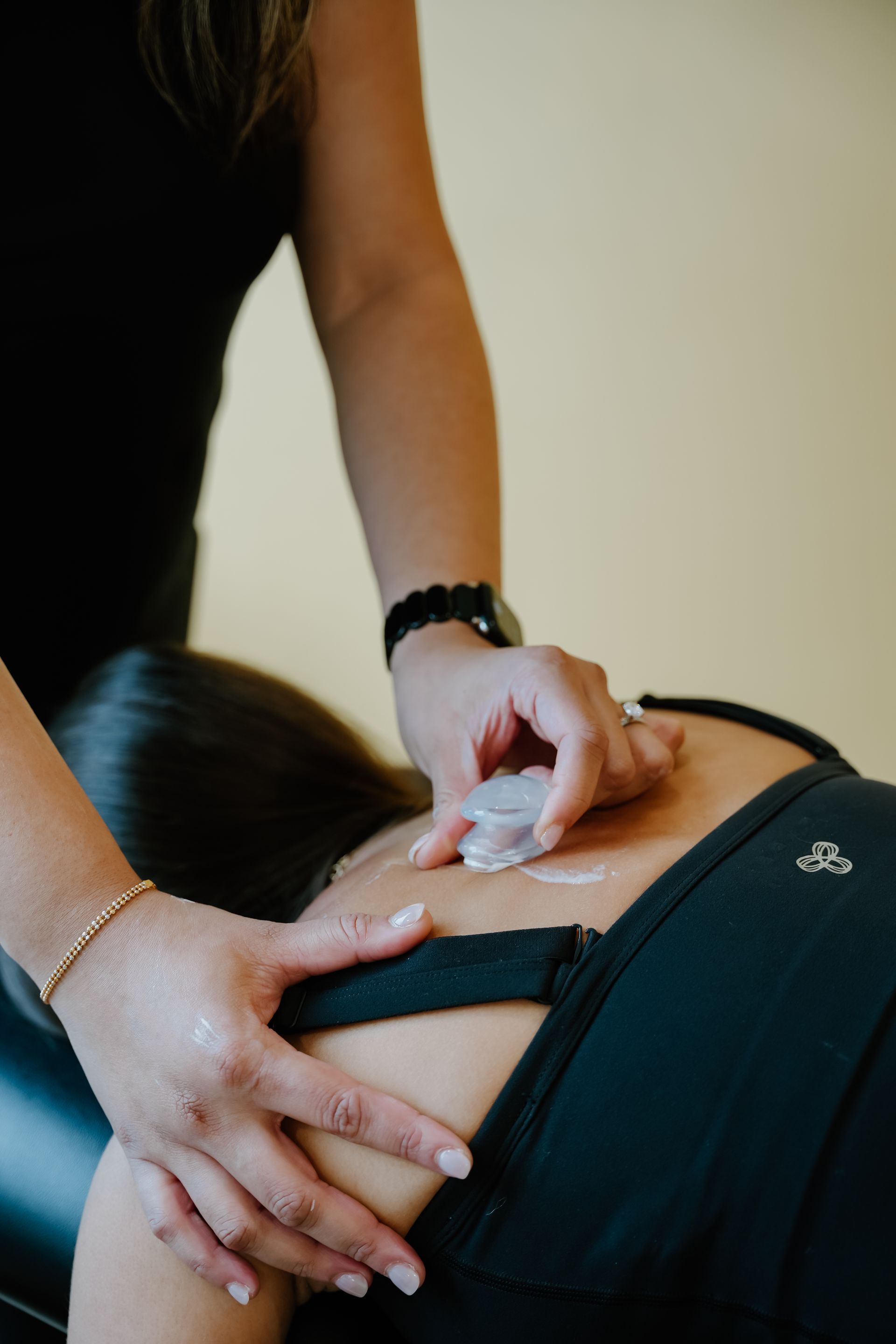 Hands using a small device on a person's bare lower back during a massage or treatment