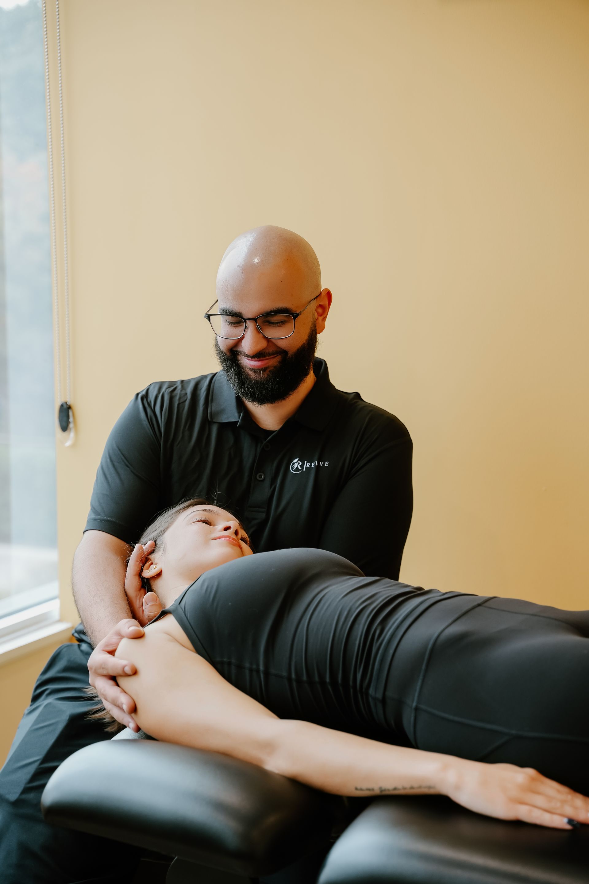 Chiropractor gently adjusting a patient lying face down on a treatment table in a bright room