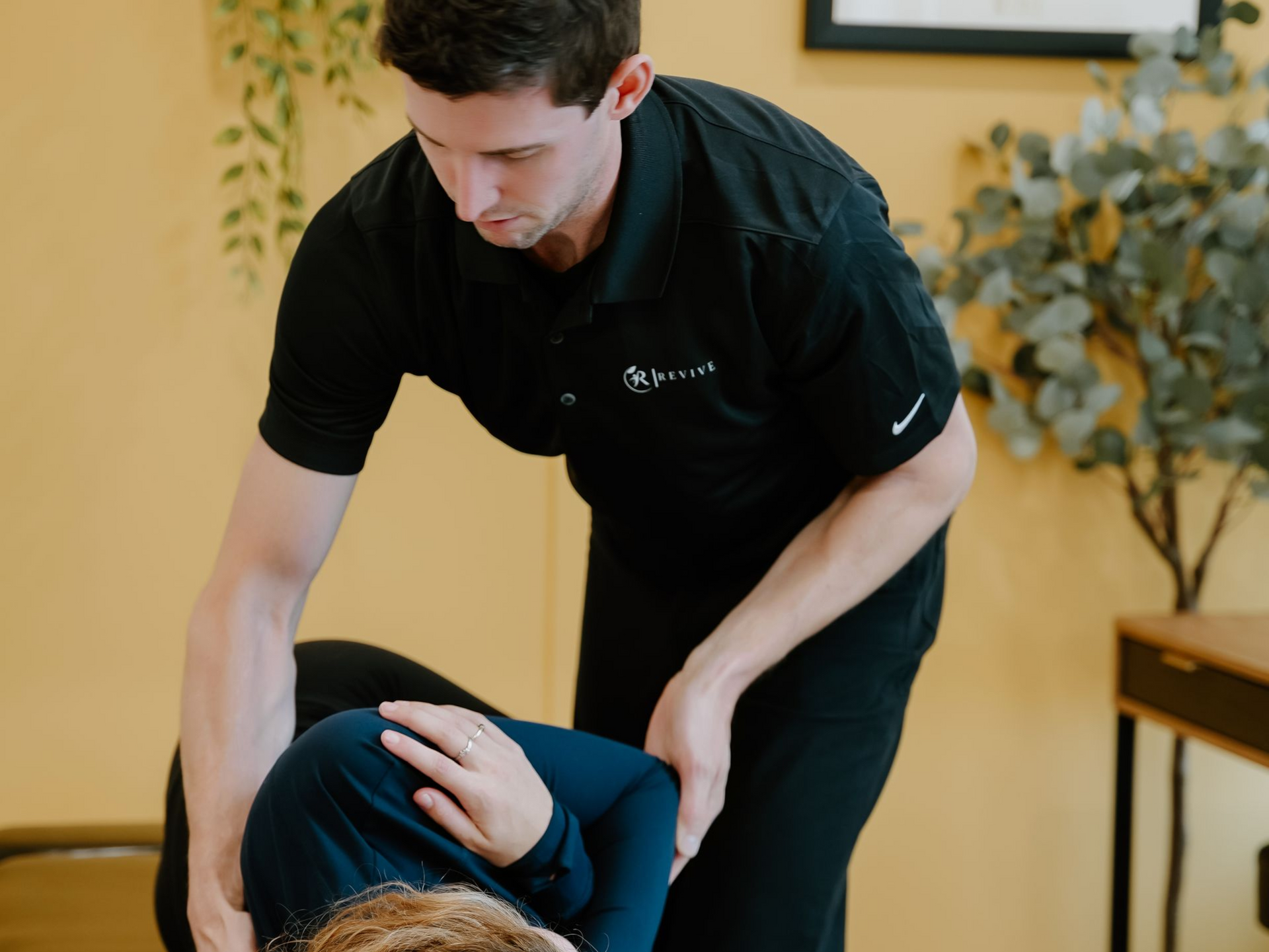 Therapist assisting a seated client in a treatment room, bending the client’s leg during a stretch