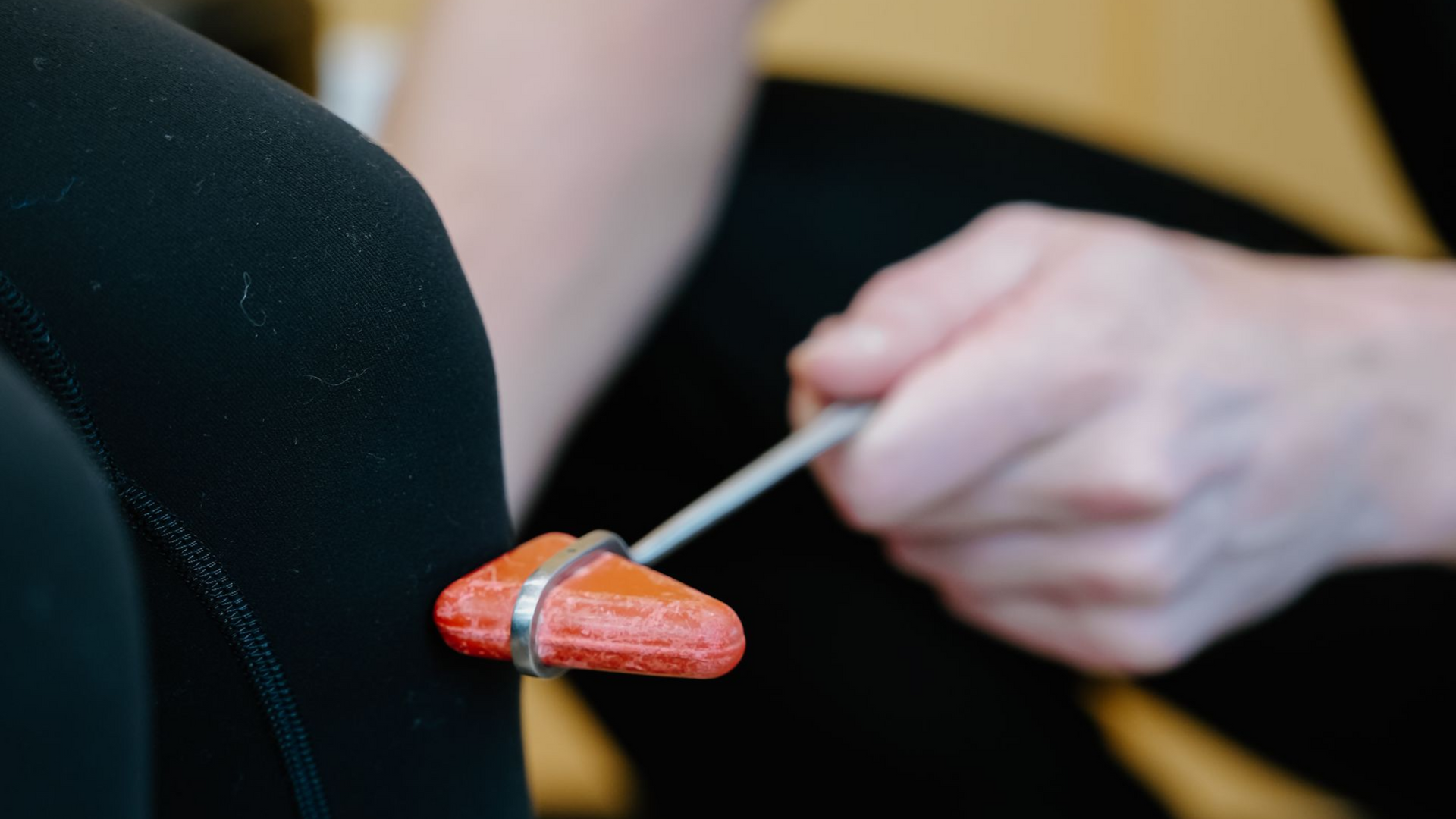 Person using a makeup brush to apply orange lipstick to a black mannequin lip