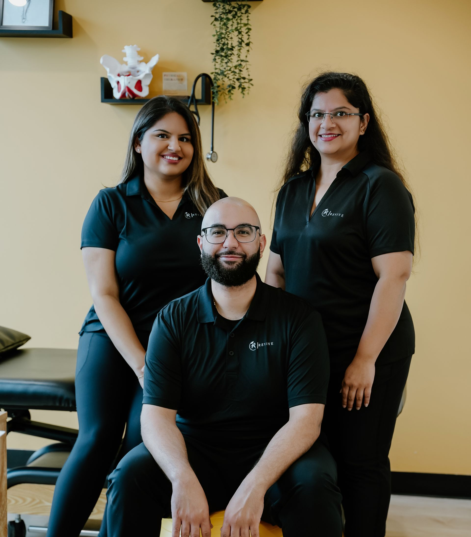 Three people in black shirts posing in an office with a yellow wall and desk behind them