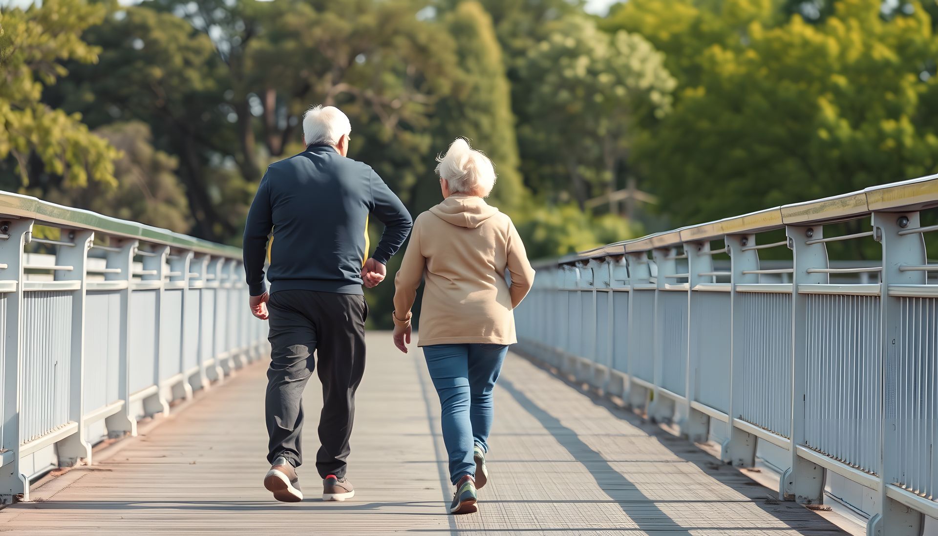 Two people walking hand in hand on a bridge with metal railings and trees in the background