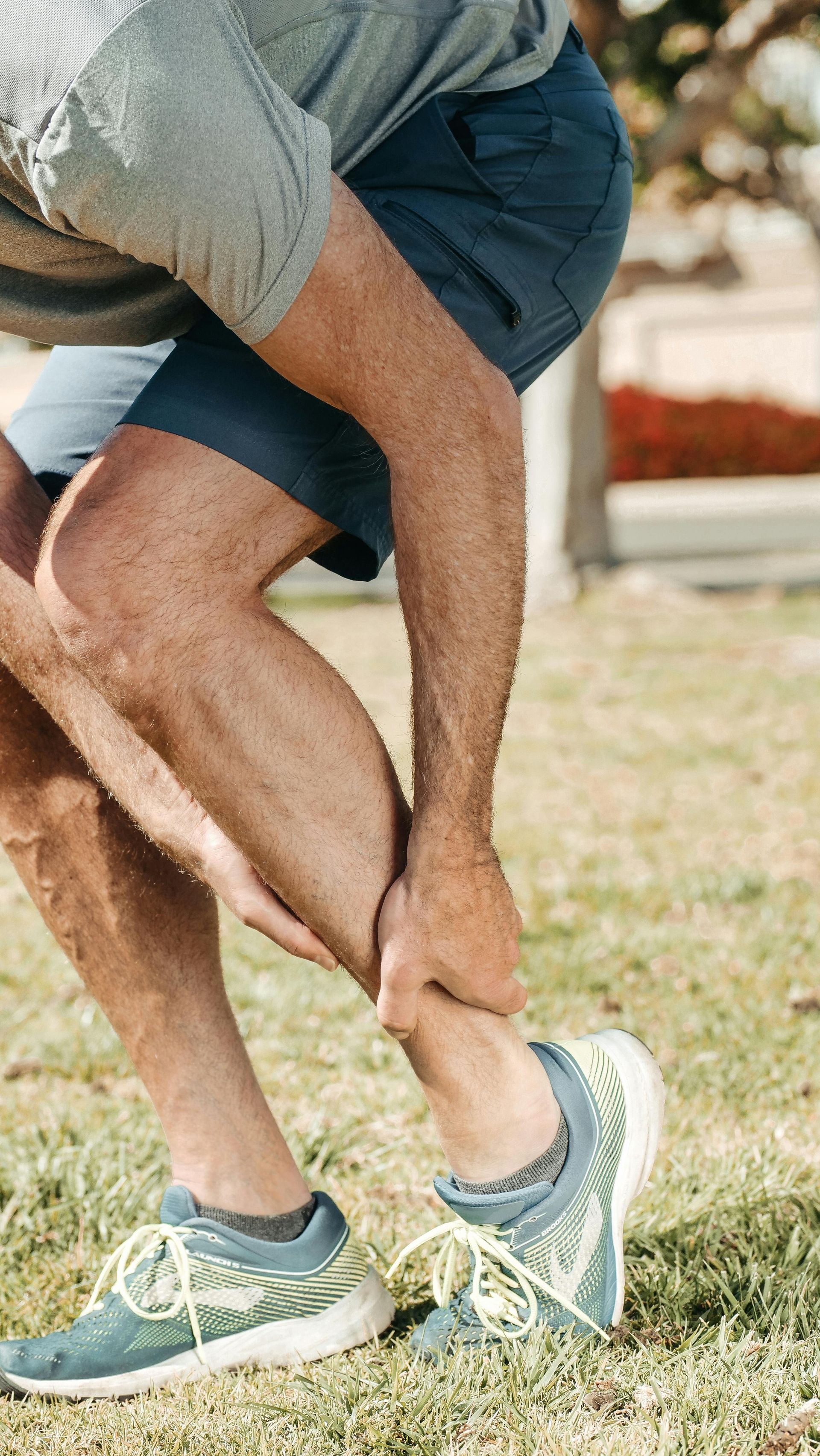 Runner bending over and clutching his calf in pain during a run outdoors