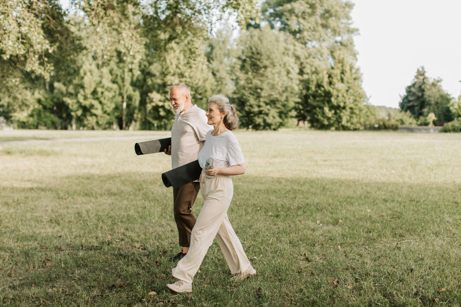 Two people walking across a grassy park, one carrying a camera with a long lens.