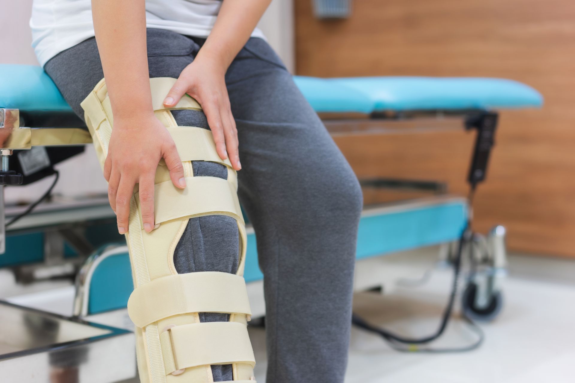 Person adjusting a beige knee brace while seated in a clinic waiting room