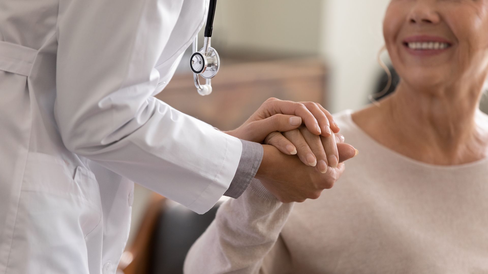 Healthcare worker holding a smiling patient’s hand in a bright clinic setting