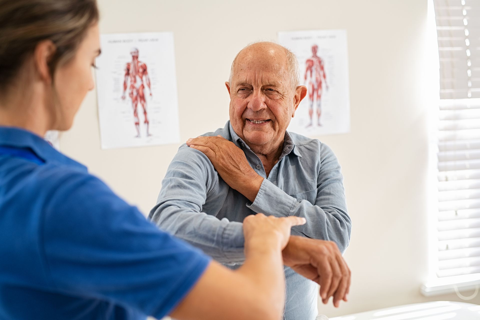 Physical therapist helping an older patient stretch his shoulder in a bright clinic room