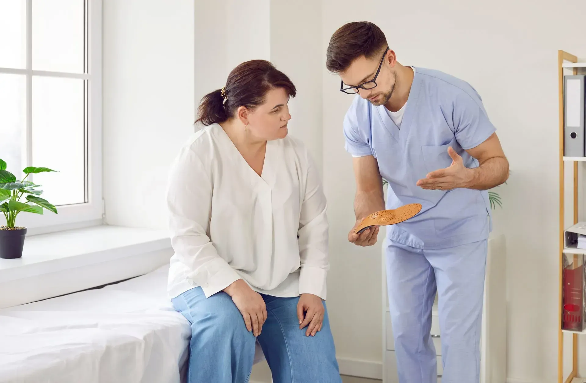Nurse in scrubs explaining a clipboard to a seated patient in a bright clinic room