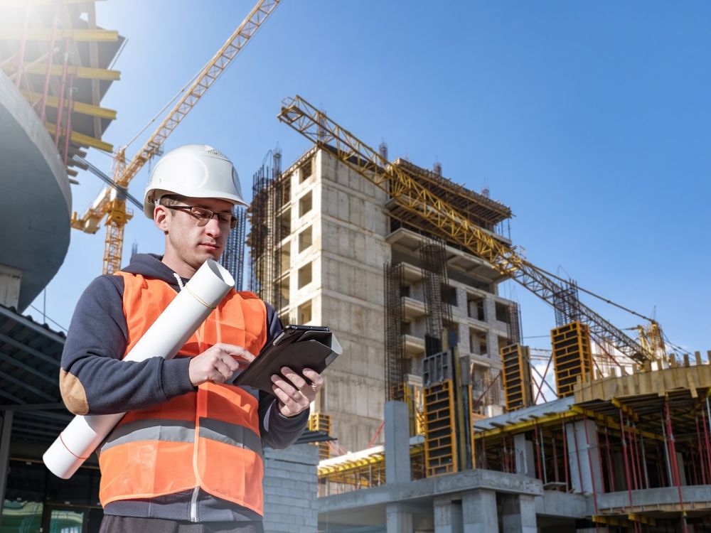 Construction worker on site, orange vest, hard hat, using tablet ...