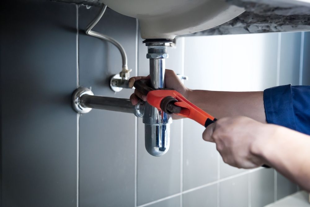 Plumber with a wrench repairing a sink's drain pipes in a bathroom.