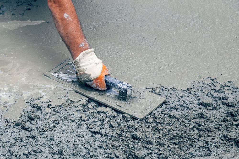 Person using a trowel to smooth wet concrete on a construction site, wearing a glove.