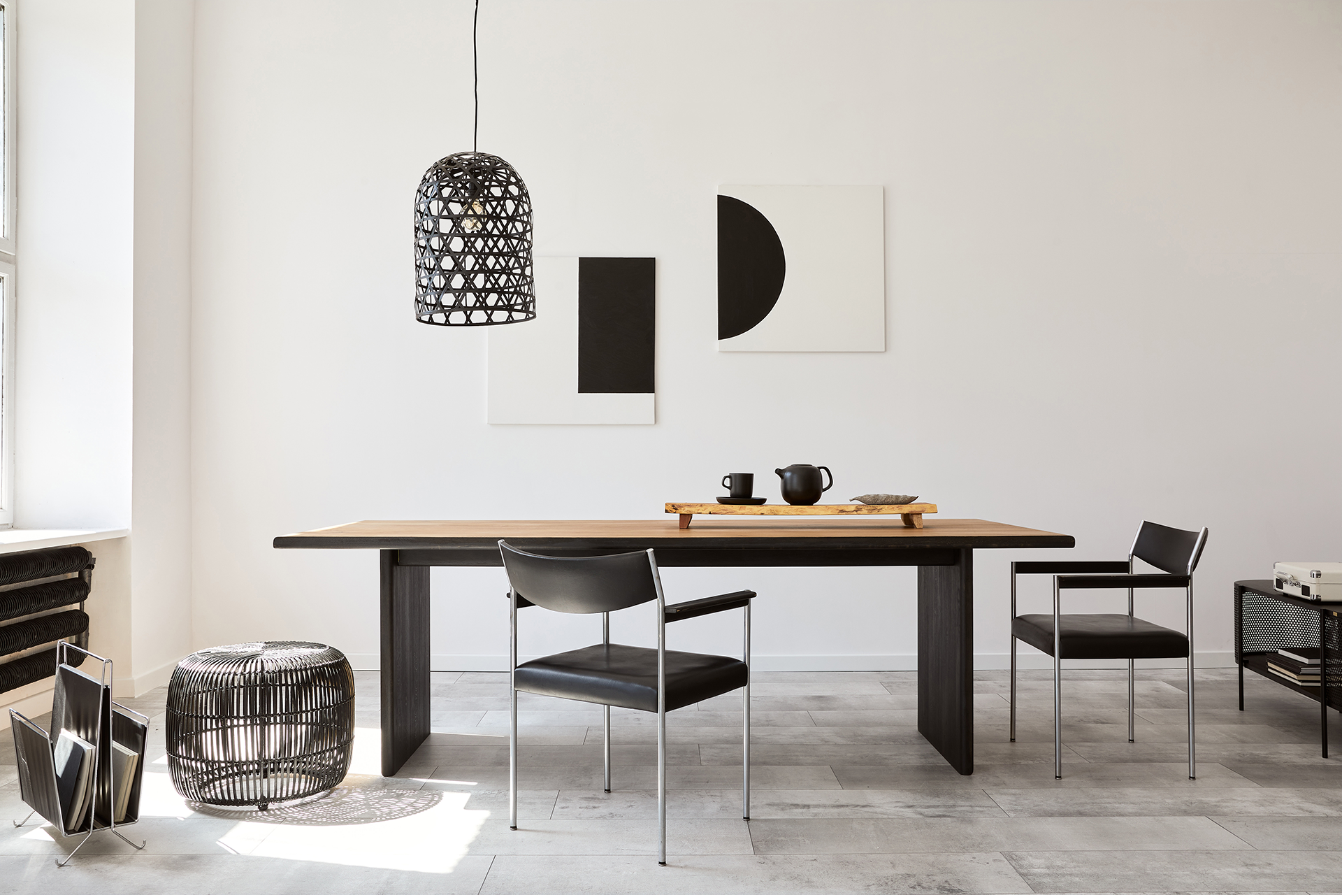 Dining room with long wooden table, black chairs, geometric art, and pendant light.