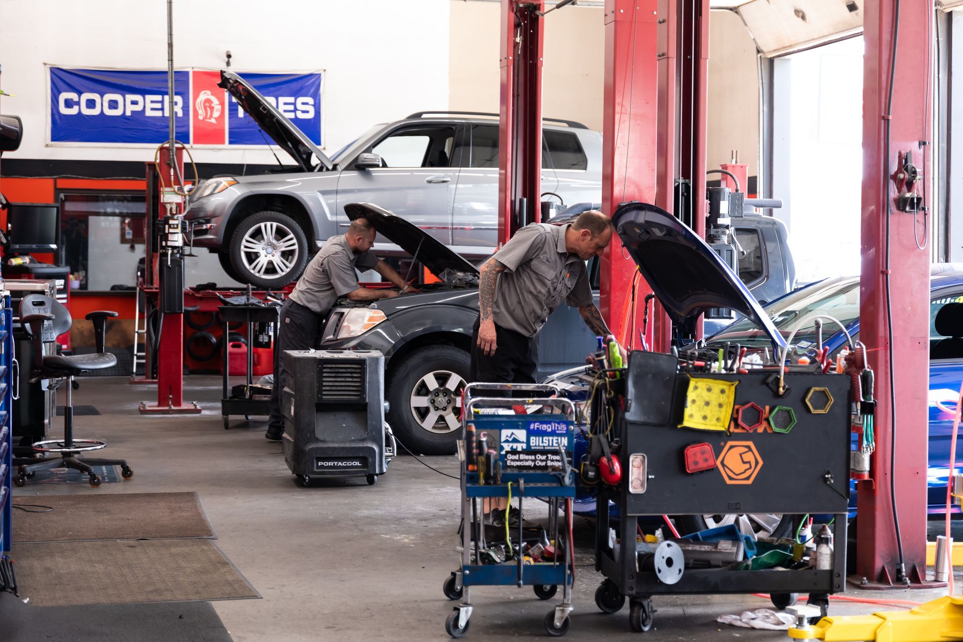 Auto repair shop with cars on lifts and mechanics working near tool carts | CarDoc Automotive