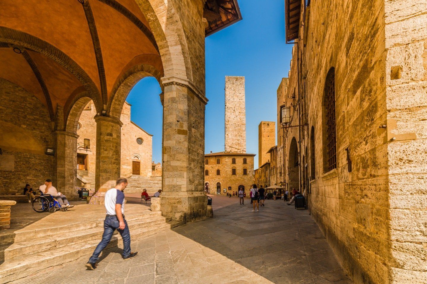 Edifici in pietra e torri a San Gimignano, Italia, con un uomo che cammina in primo piano.