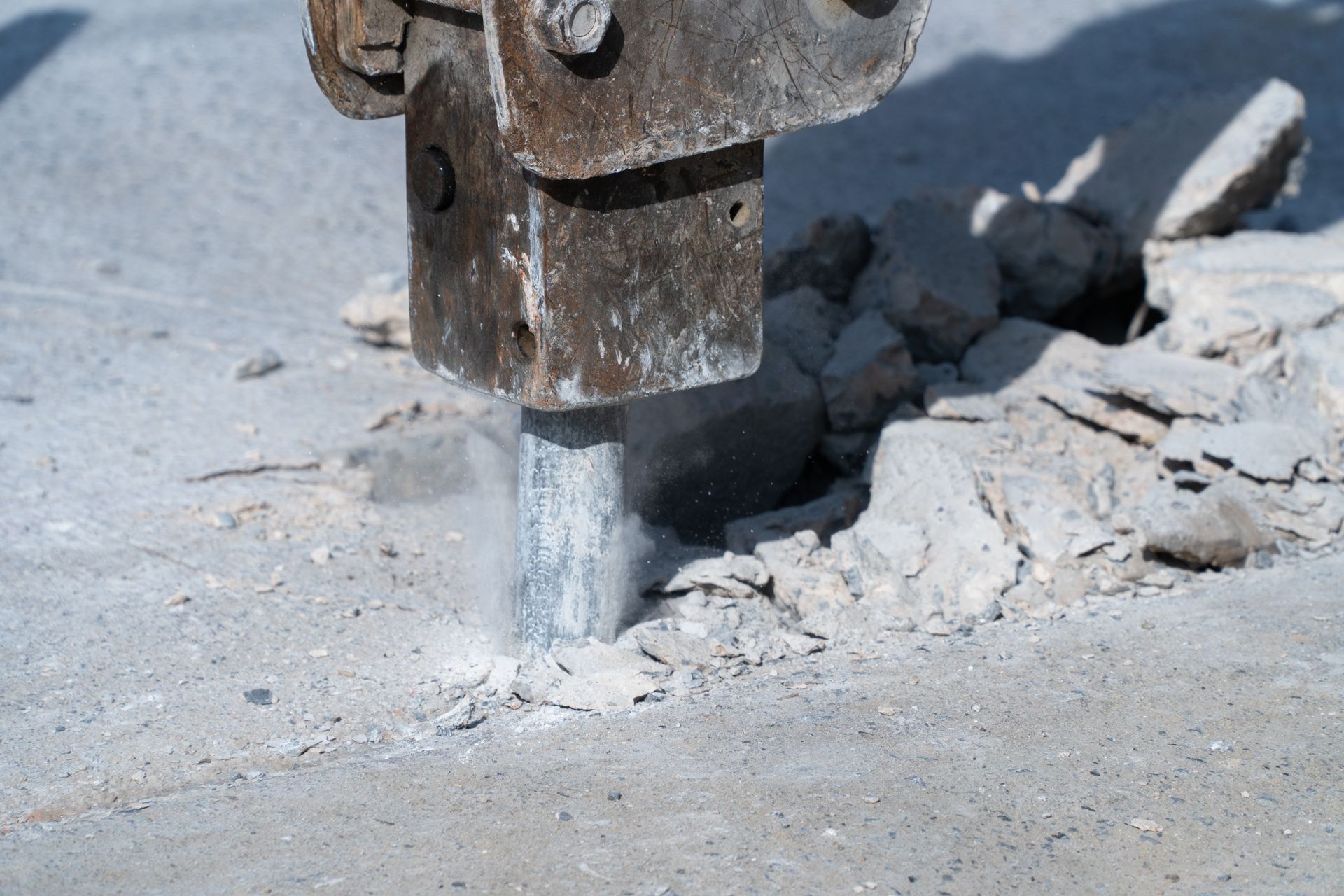 A close-up of a hydraulic jackhammer being drilled into a cement road.