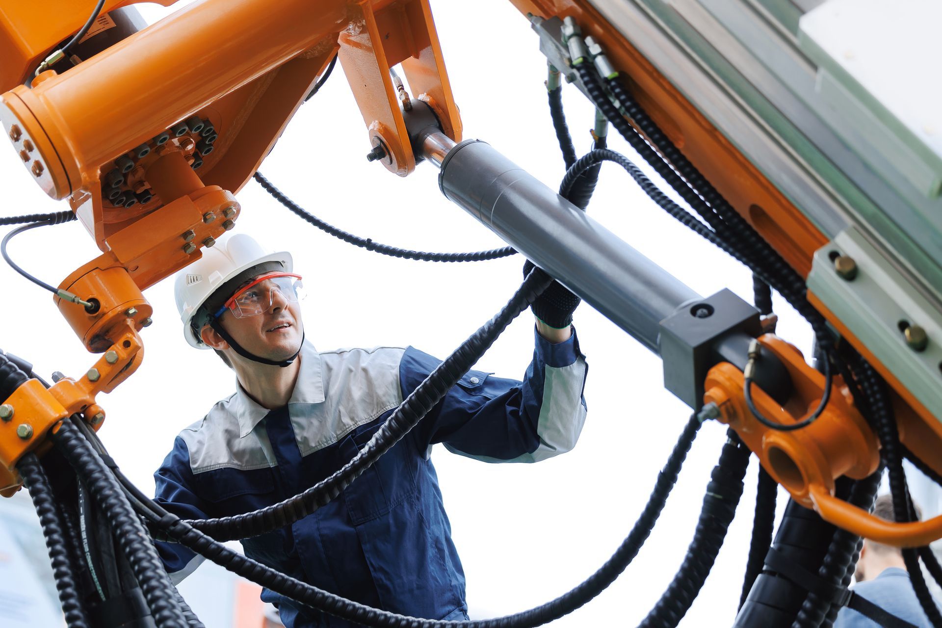 Engineer wearing a helmet and protection glasses inspecting hydraulic hoses of heavy machinery.