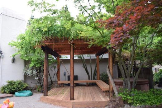 Wooden gazebo with built-in seating, surrounded by greenery and trees.