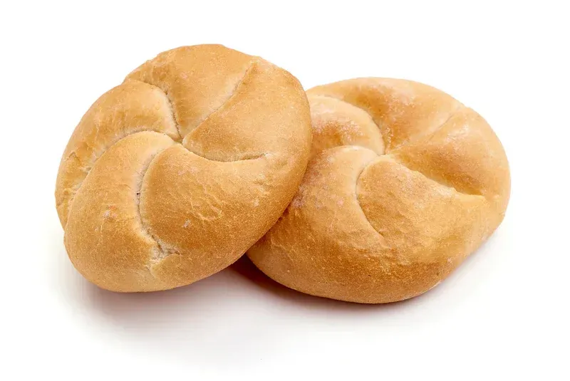 A basket filled with rolls and wheat ears on a table.