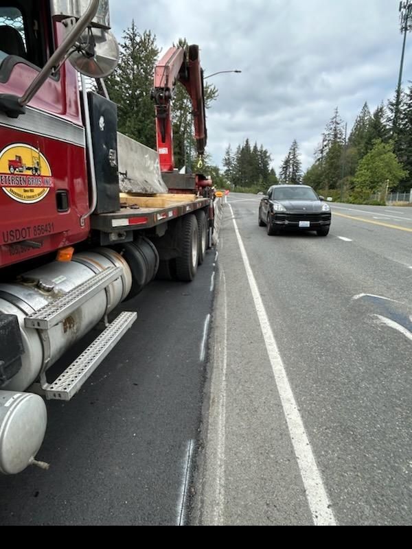 Red truck with crane lifting a concrete barrier on a road with a car. Cloudy day.
